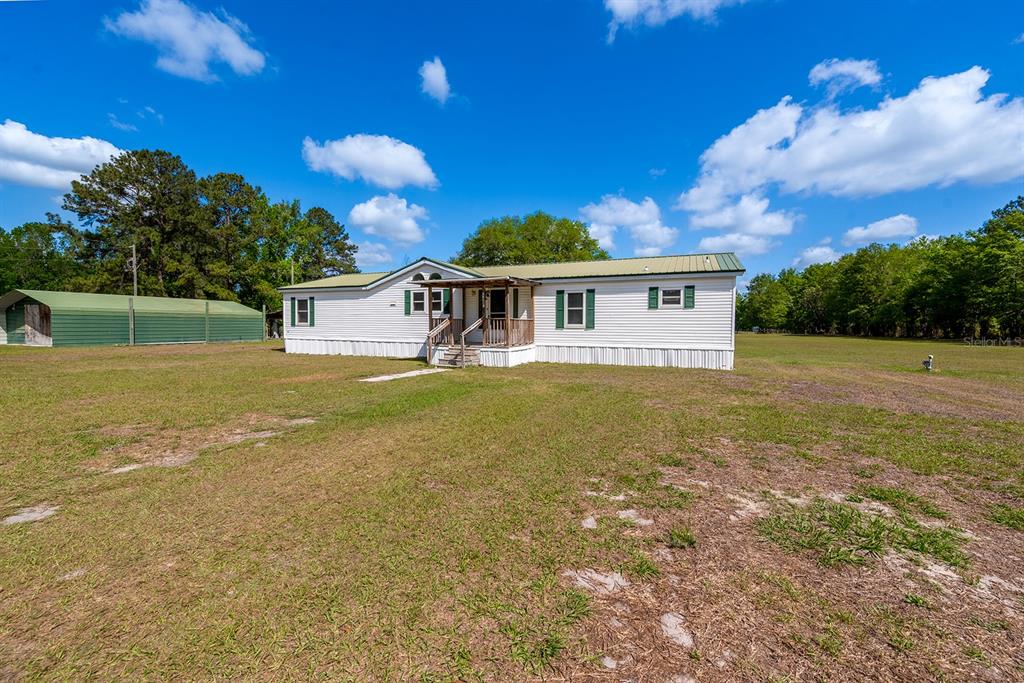 A white manufactured home with a green metal roof sits on a large grassy lot — 11201 SW 49TH TERRACE, LAKE BUTLER, FL