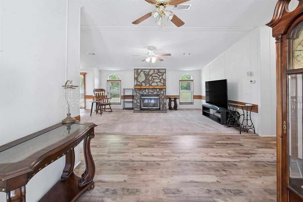 A living room features a stone fireplace, carpeted flooring, and a wood-look laminate entryway — 11201 SW 49TH TERRACE, LAKE BUTLER, FL