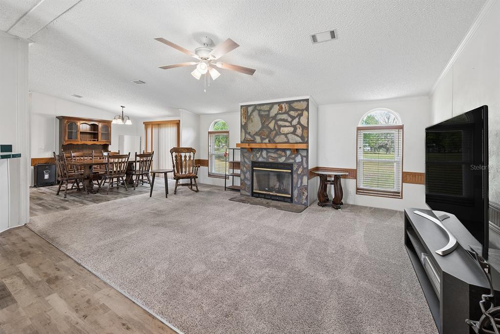 A living room with carpet, a stone fireplace, and an adjacent dining area — 11201 SW 49TH TERRACE, LAKE BUTLER, FL