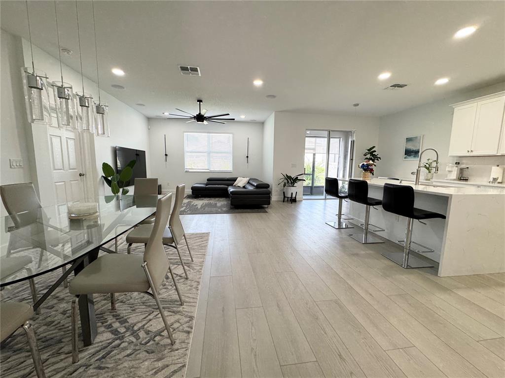 An open-concept living and dining area features light wood flooring, a glass table, and kitchen island — 3078 MARINE GRASS DRIVE, WIMAUMA, FL