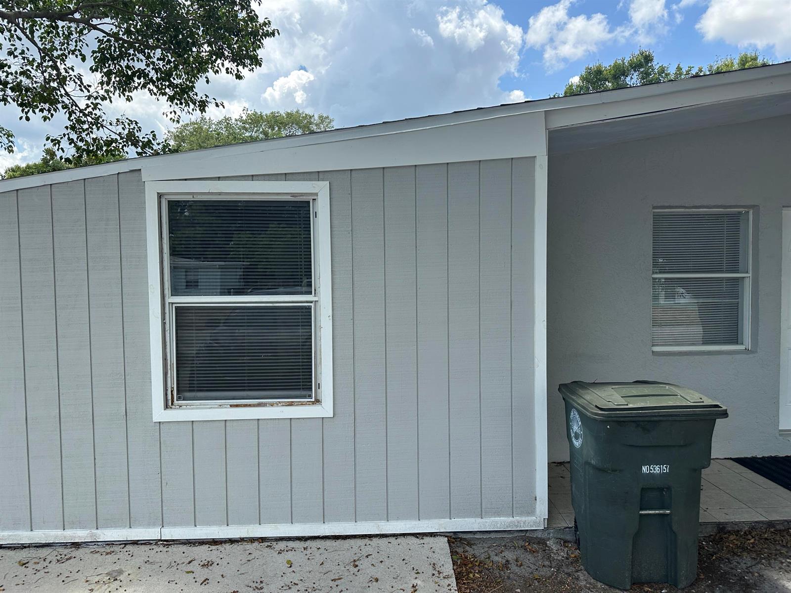 The exterior of a gray house features vertical siding, a window, and a trash bin — 115 Maple Avenue, Fort Pierce FL 34982, FORT PIERCE, FL