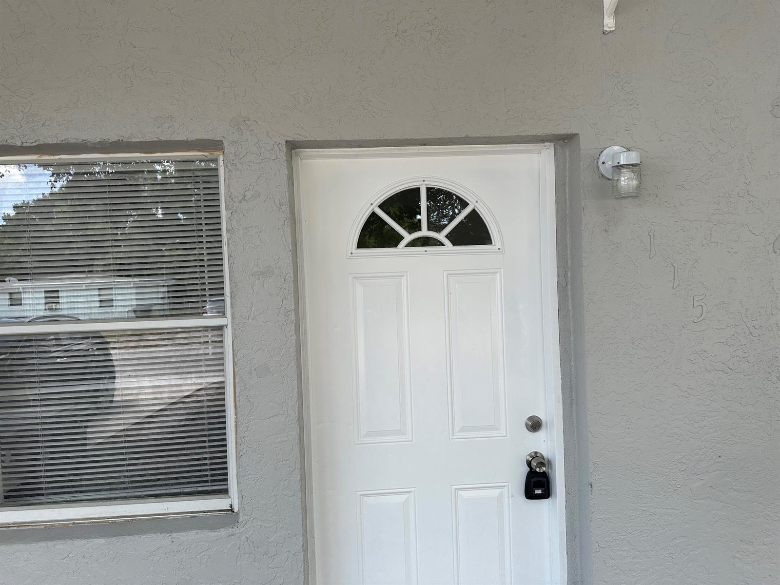 A white front door with a semi-circular window sits next to a window with blinds — 115 Maple Avenue, Fort Pierce FL 34982, FORT PIERCE, FL