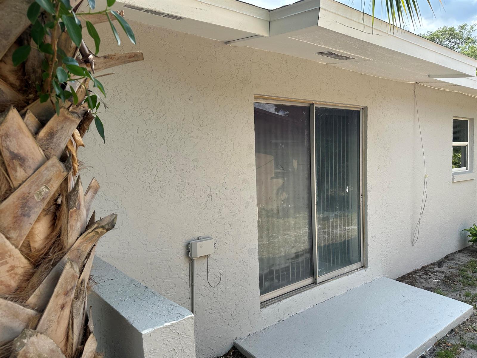 An exterior view of a house with a sliding glass door, stucco walls, and patio — 115 Maple Avenue, Fort Pierce FL 34982, FORT PIERCE, FL