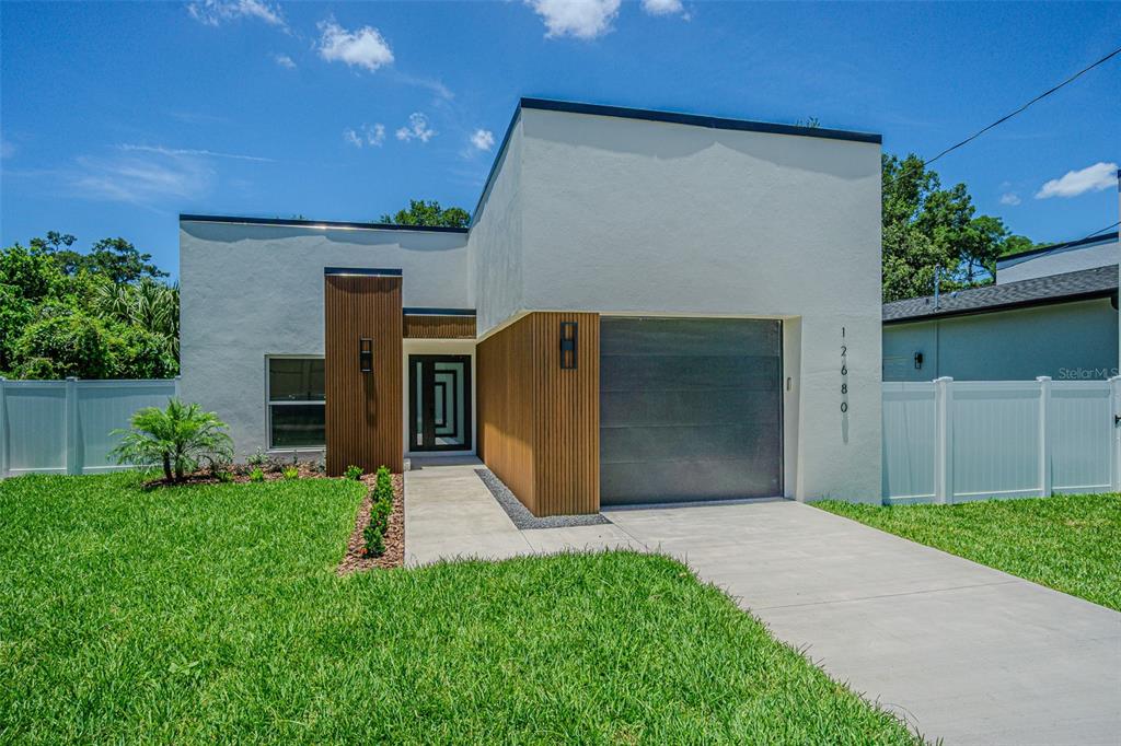 A modern, white single-story house features wood-slat accents, a gray garage door, and a driveway — 12680 N CENTRAL AVENUE, TAMPA, FL