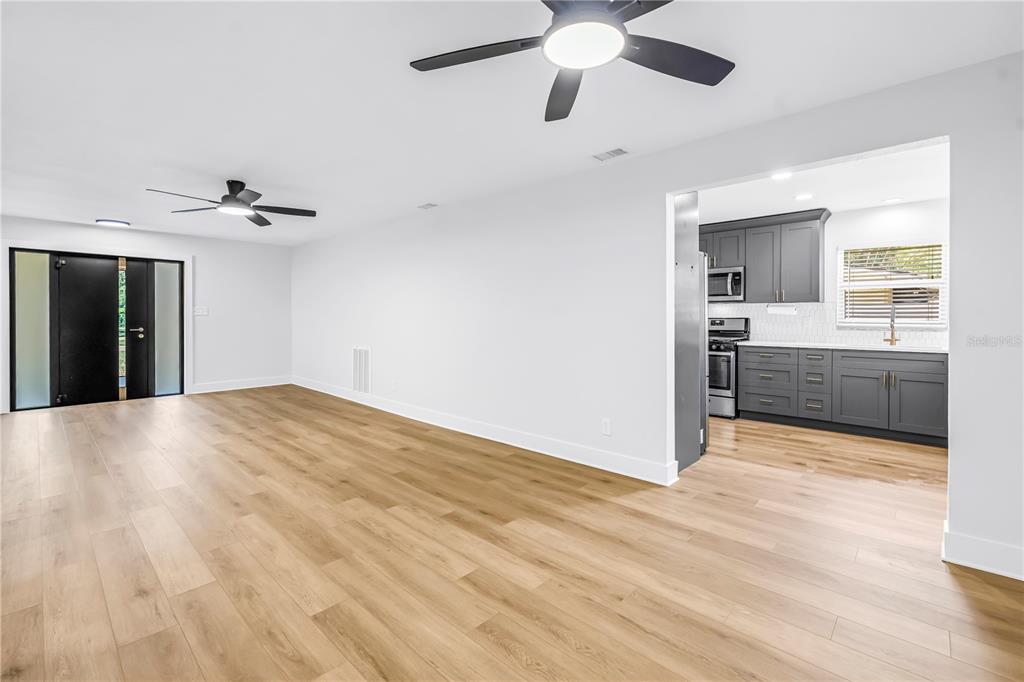 A living room with light wood flooring leads to a kitchen with dark gray cabinets — 5846 12TH STREET S, ST PETERSBURG, FL