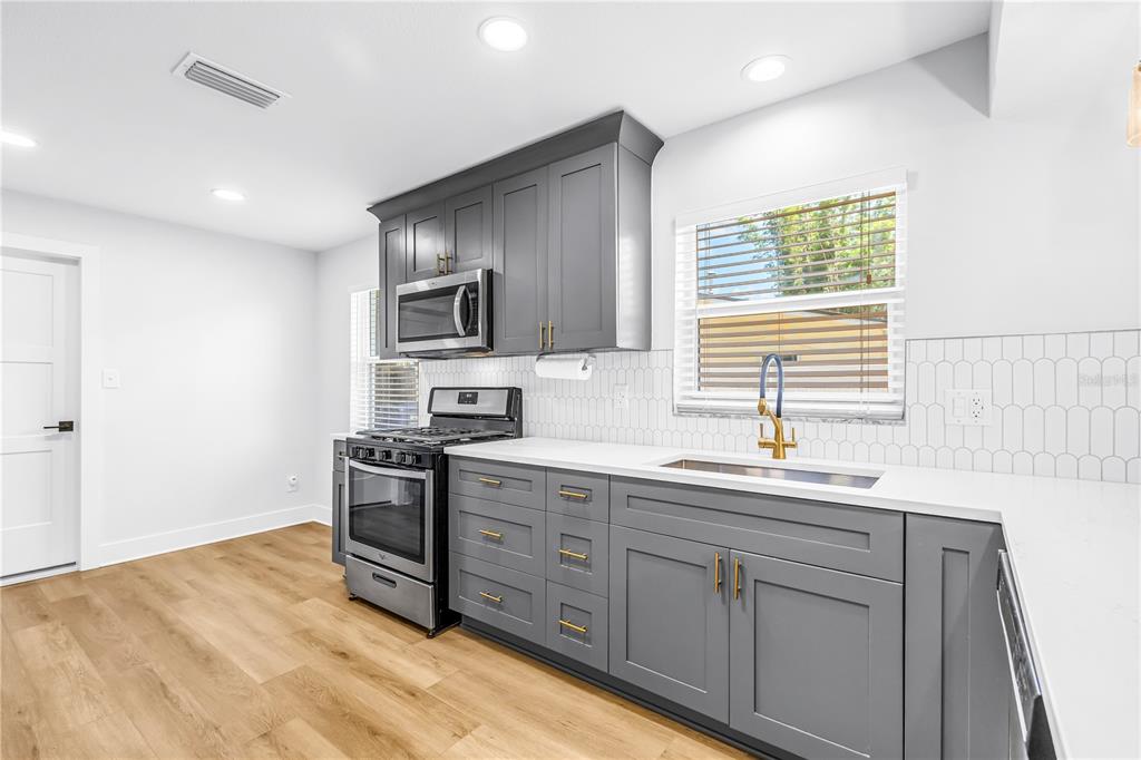 A kitchen features gray cabinets, white countertops, stainless steel appliances, and a white tiled backsplash — 5846 12TH STREET S, ST PETERSBURG, FL