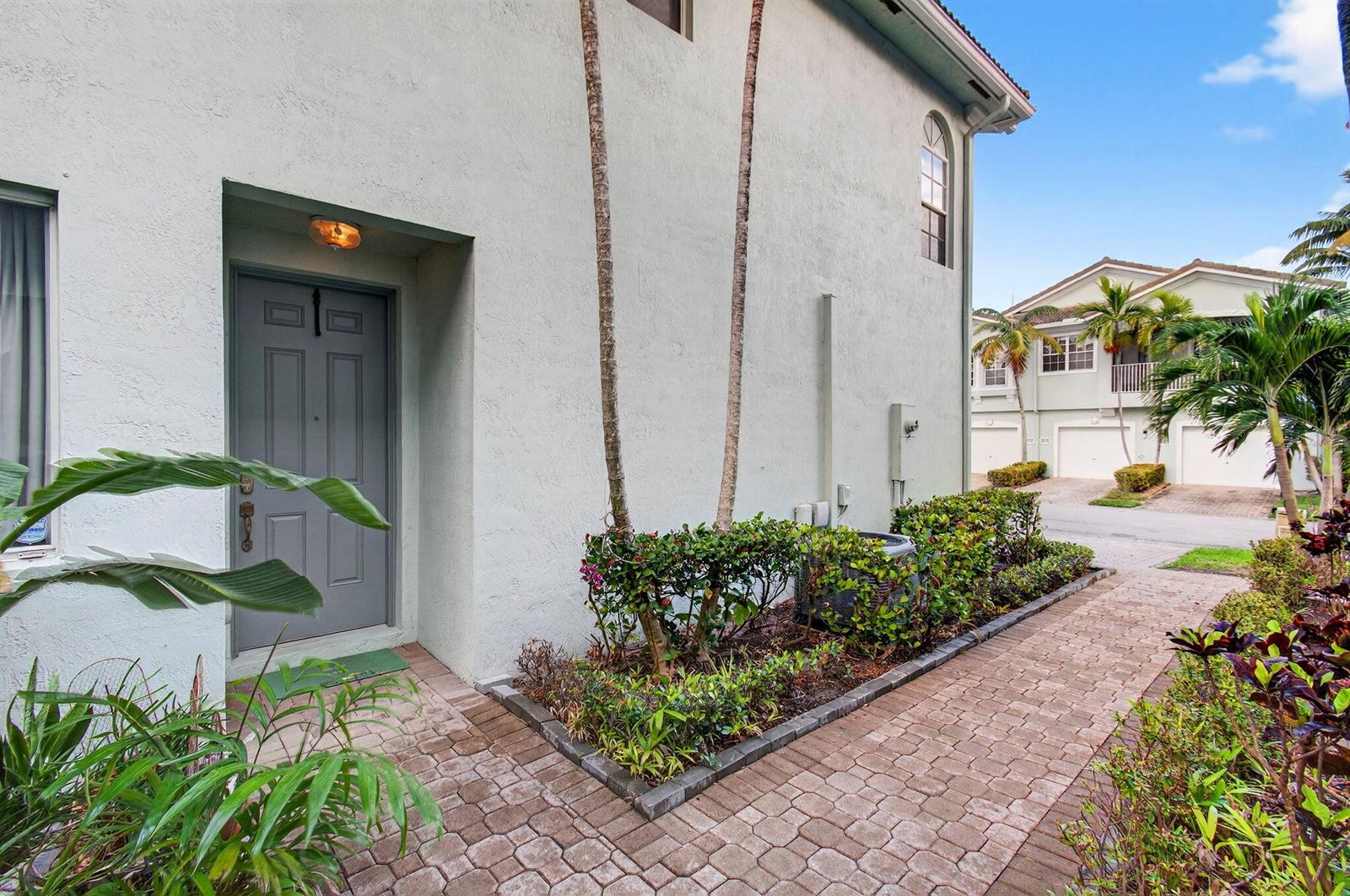 A gray front door is set into a light-colored stucco exterior with a brick walkway — 3167 Laurel Ridge Circle, Riviera Beach FL 33404, RIVIERA BEACH, FL