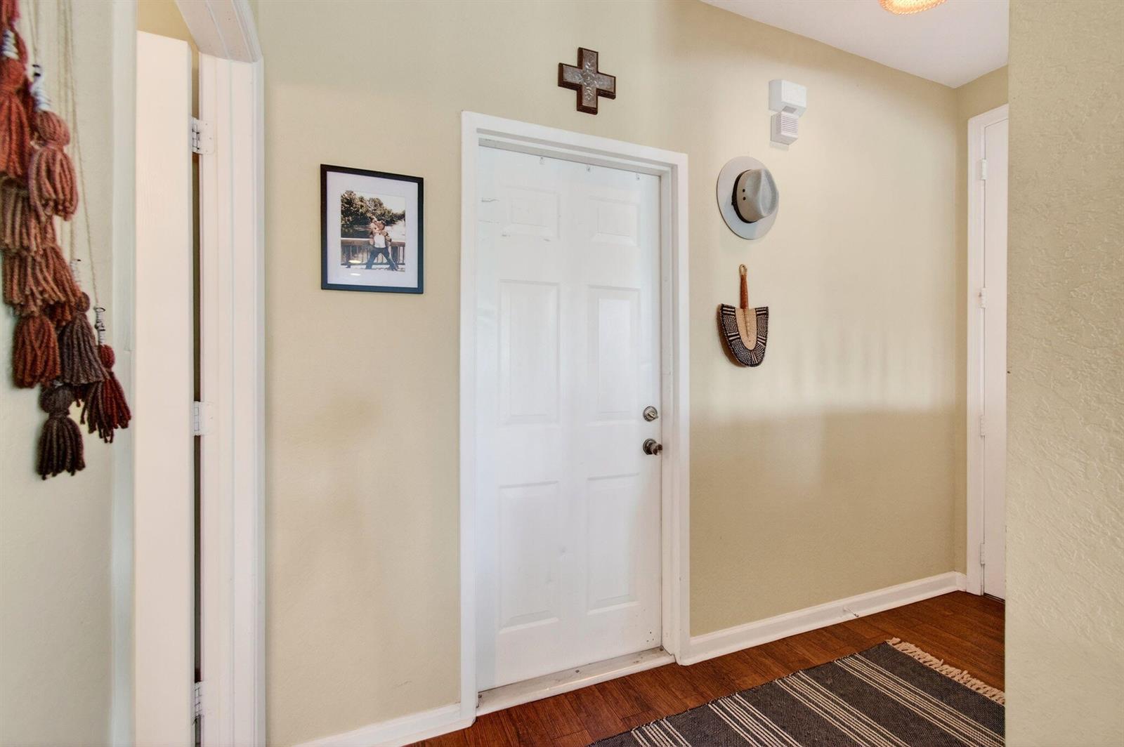 A hallway features a white door, a framed photo, wall decor, and wood flooring — 3167 Laurel Ridge Circle, Riviera Beach FL 33404, RIVIERA BEACH, FL