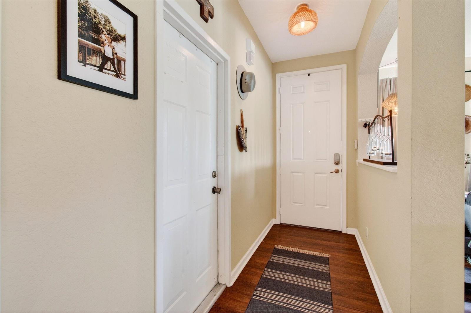 A hallway with wood-look flooring, two white doors, a light fixture, and a striped rug — 3167 Laurel Ridge Circle, Riviera Beach FL 33404, RIVIERA BEACH, FL