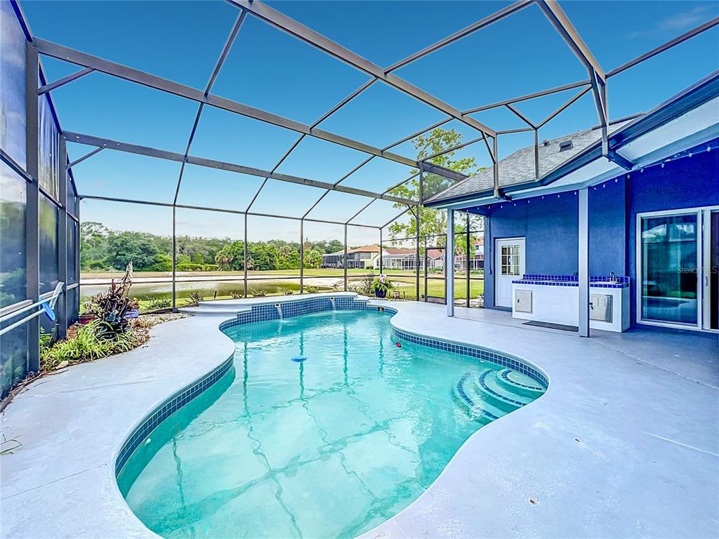 A swimming pool with a raised spa sits inside a screened-in lanai overlooking a pond — 1104 NEEDLEWOOD LOOP, OVIEDO, FL
