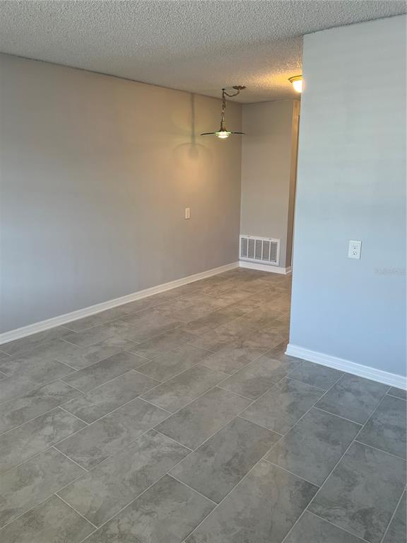 An empty room with gray tile flooring, light gray walls, and a hanging pendant light — 4945 ELKNER STREET, NEW PORT RICHEY, FL