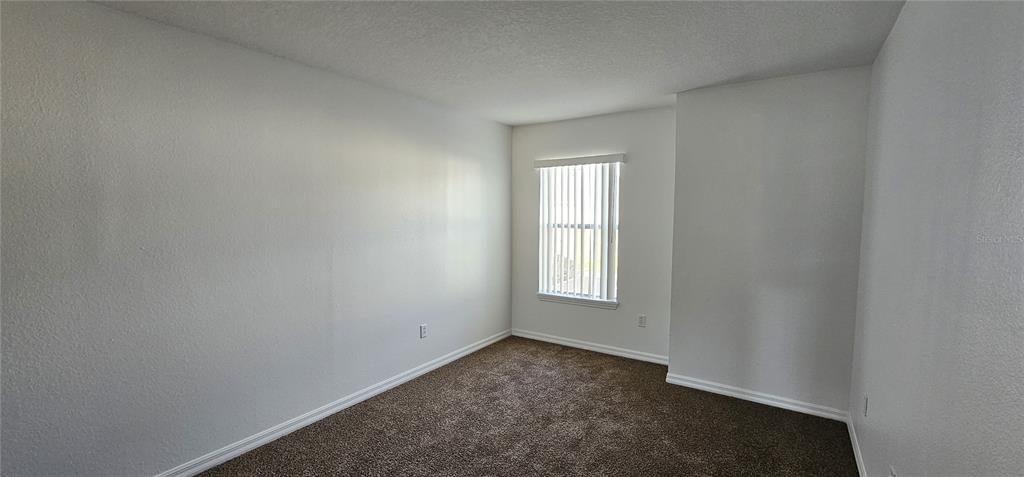 An empty bedroom with white walls, brown carpet, and a window with vertical blinds — 2836 CLUB CORTILE CIRCLE, KISSIMMEE, FL