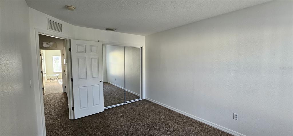 An empty bedroom features brown carpet, white walls, a closet with mirrored doors, and an open doorway — 2836 CLUB CORTILE CIRCLE, KISSIMMEE, FL
