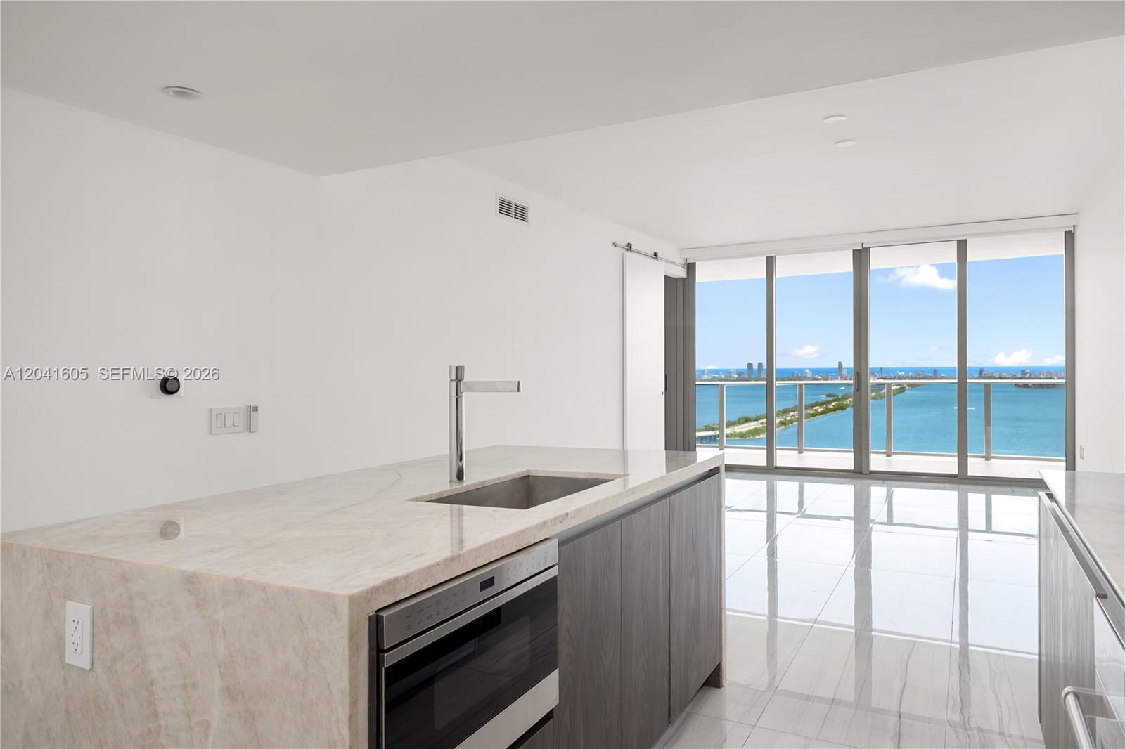 A modern kitchen island with a stone countertop faces floor-to-ceiling windows overlooking the ocean — 3131 NE 7th Ave # 4102, Miami FL 33137, MIAMI, FL