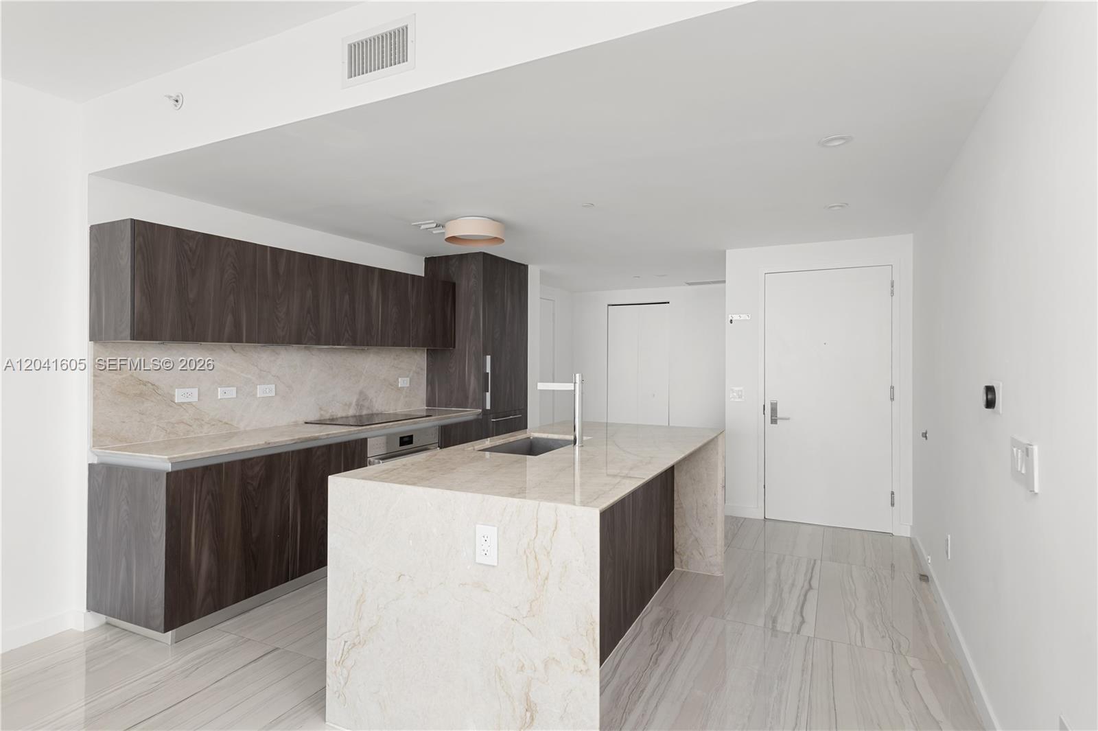 A modern kitchen features dark wood cabinetry, marble countertops, and a large central island — 3131 NE 7th Ave # 4102, Miami FL 33137, MIAMI, FL