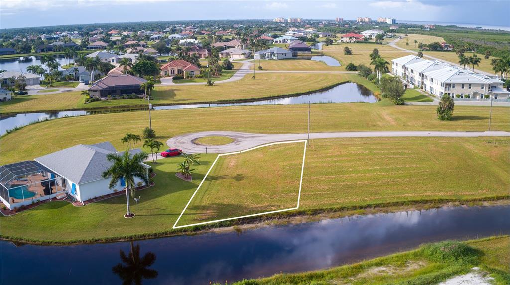 An aerial view shows a vacant residential lot outlined in white next to a canal — 24070 CHERRYSTONE LANE, PUNTA GORDA, FL