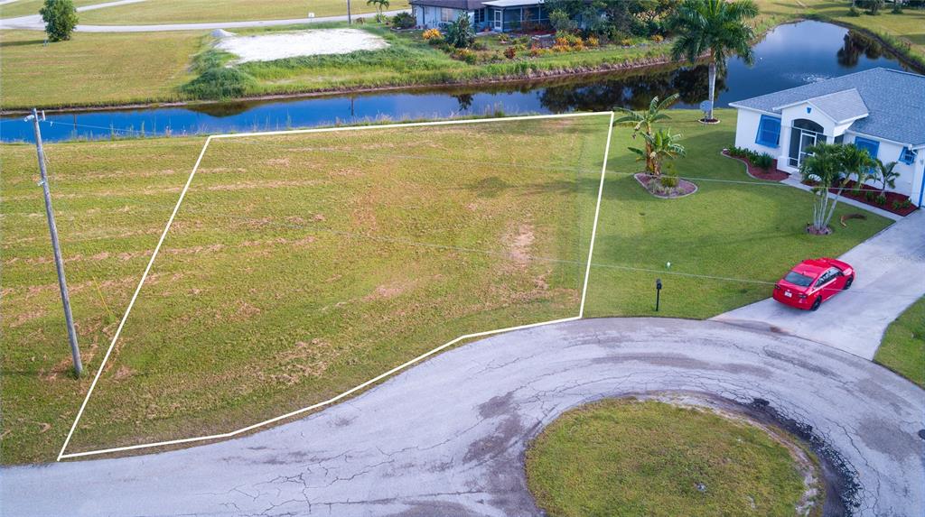 An aerial view shows a vacant, trapezoidal residential lot situated next to a house — 24070 CHERRYSTONE LANE, PUNTA GORDA, FL