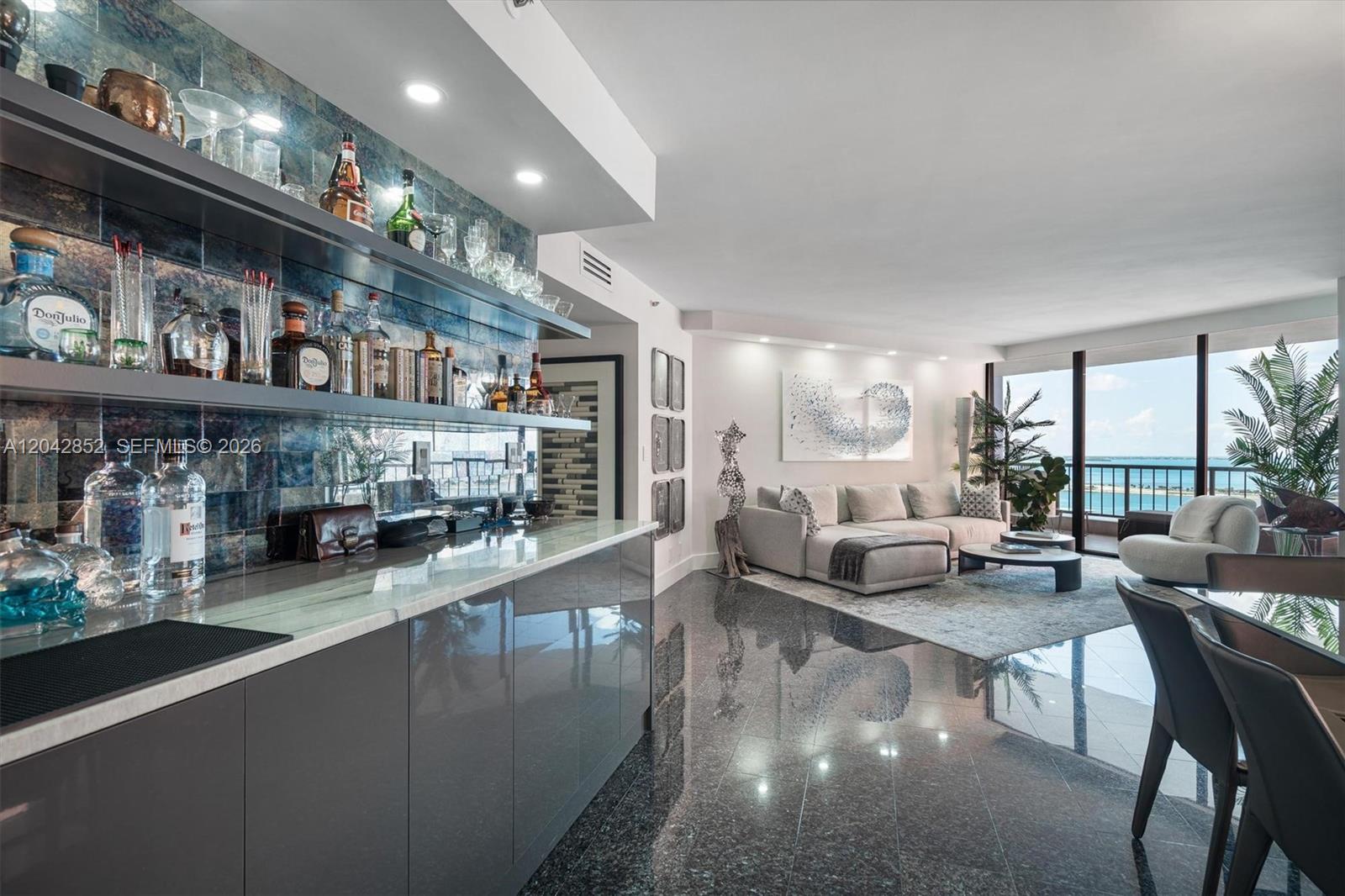 A modern living room features a wet bar with dark cabinetry and a scenic balcony view — 1581 Brickell Ave # 1805, Miami FL 33129, MIAMI, FL
