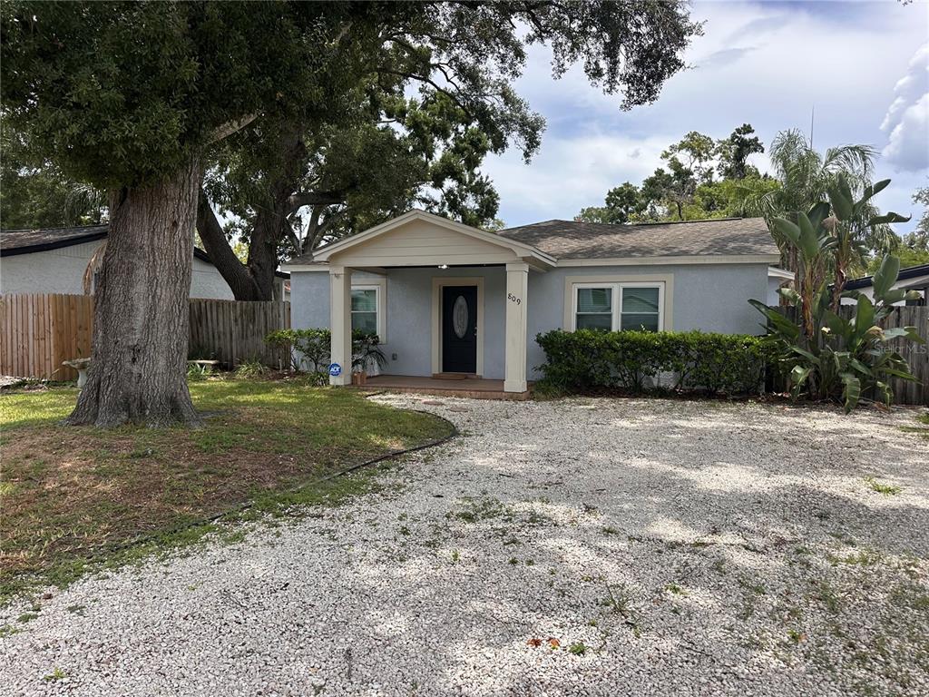 A light blue single-story house features a gravel driveway, a covered porch, and large trees — 809 W HIAWATHA STREET, TAMPA, FL