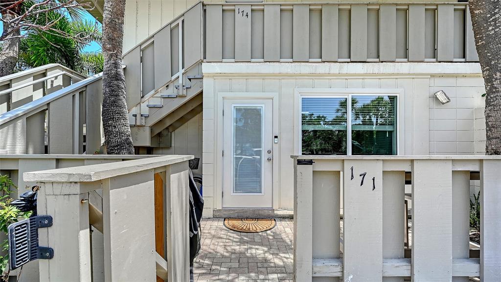 The exterior of a two-story building features a white door, a window, and wooden fencing — 6750 GULF OF MEXICO DRIVE UNIT 171, LONGBOAT KEY, FL