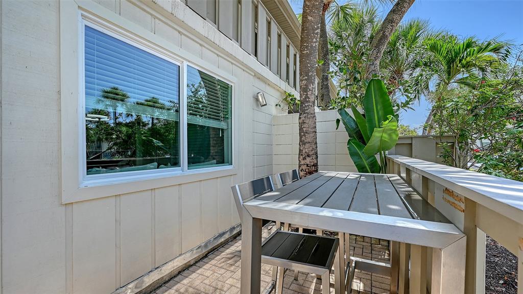 A patio with a metal table and chairs sits beside a building with a large window — 6750 GULF OF MEXICO DRIVE UNIT 171, LONGBOAT KEY, FL