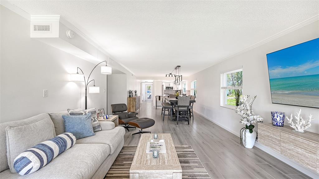 A bright living room features light wood flooring, a gray sofa, and an open dining area — 6750 GULF OF MEXICO DRIVE UNIT 171, LONGBOAT KEY, FL