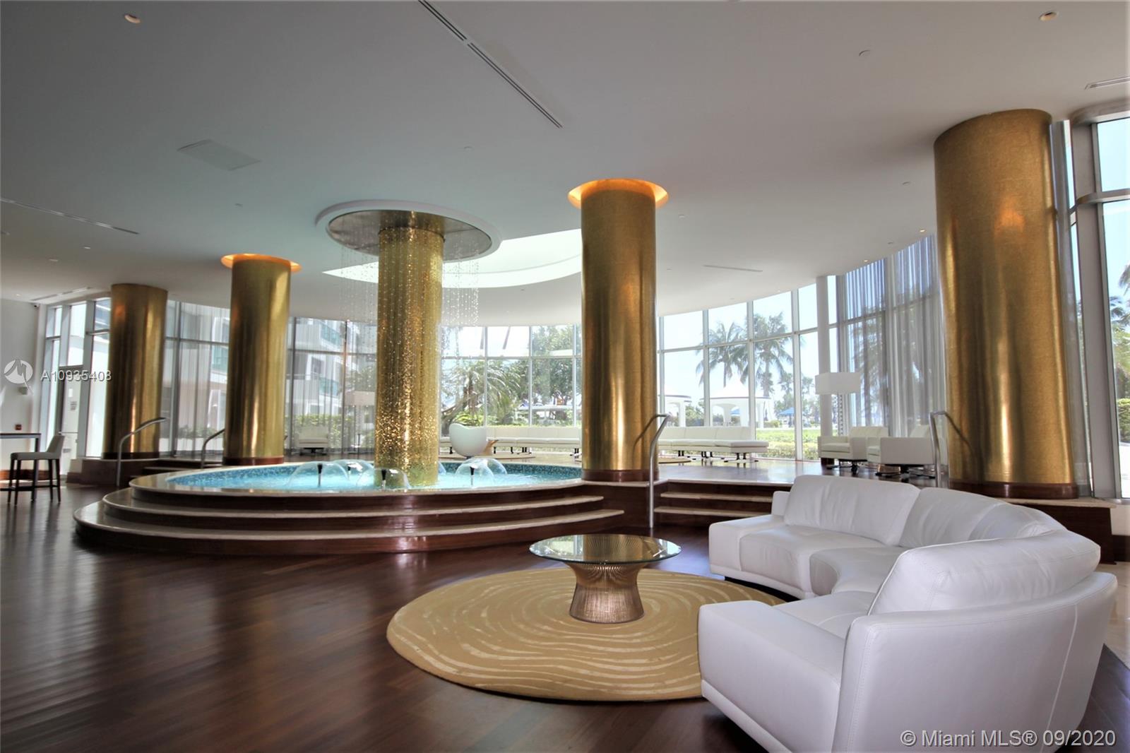 A modern lobby features a central circular fountain, gold columns, and white leather seating — 5161 COLLINS AV # 508, Miami Beach FL 33140, MIAMI BEACH, FL