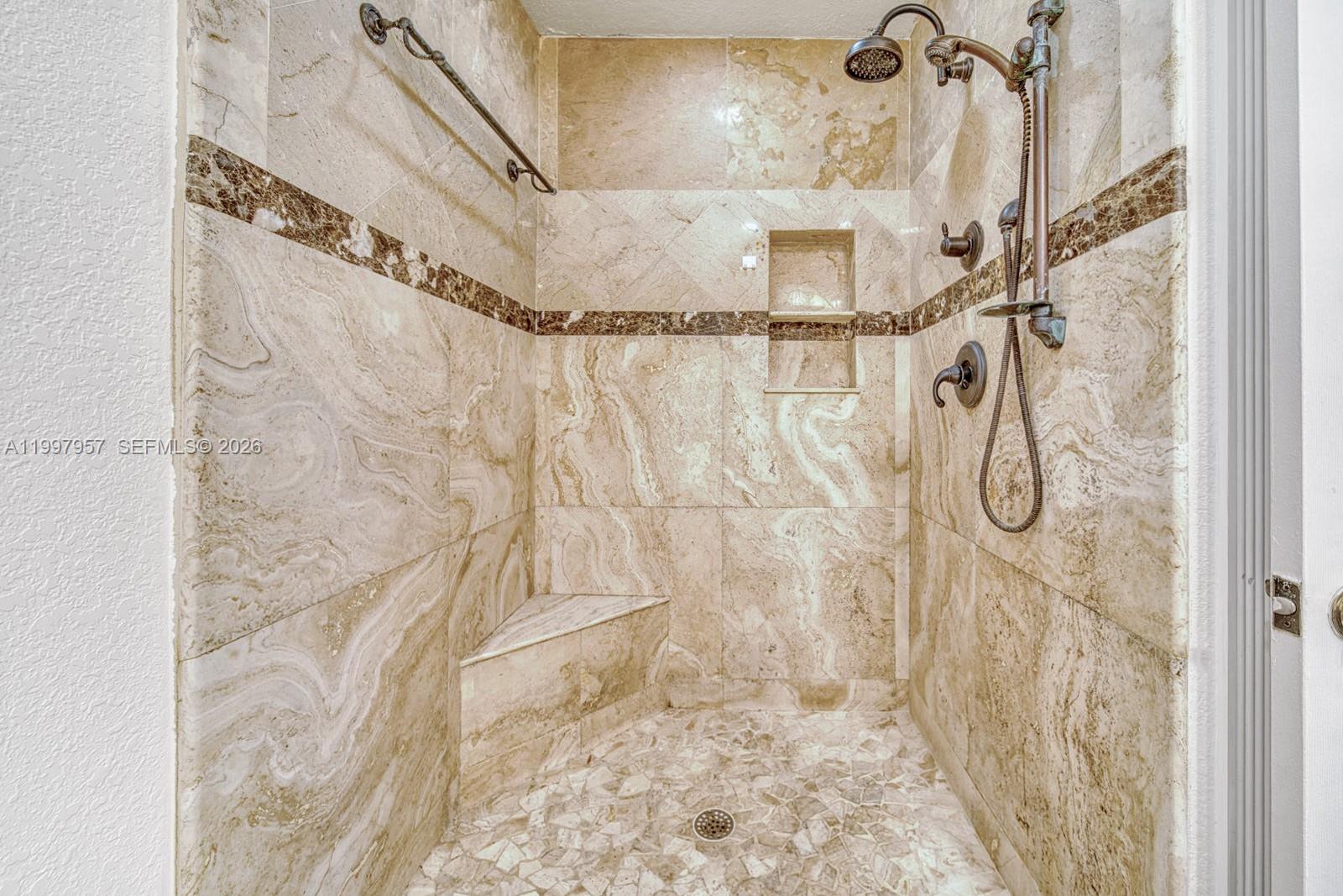 A walk-in shower features beige marble tile walls, a corner bench, and bronze fixtures — 2171 SW 21st St, Miami FL 33145, MIAMI, FL