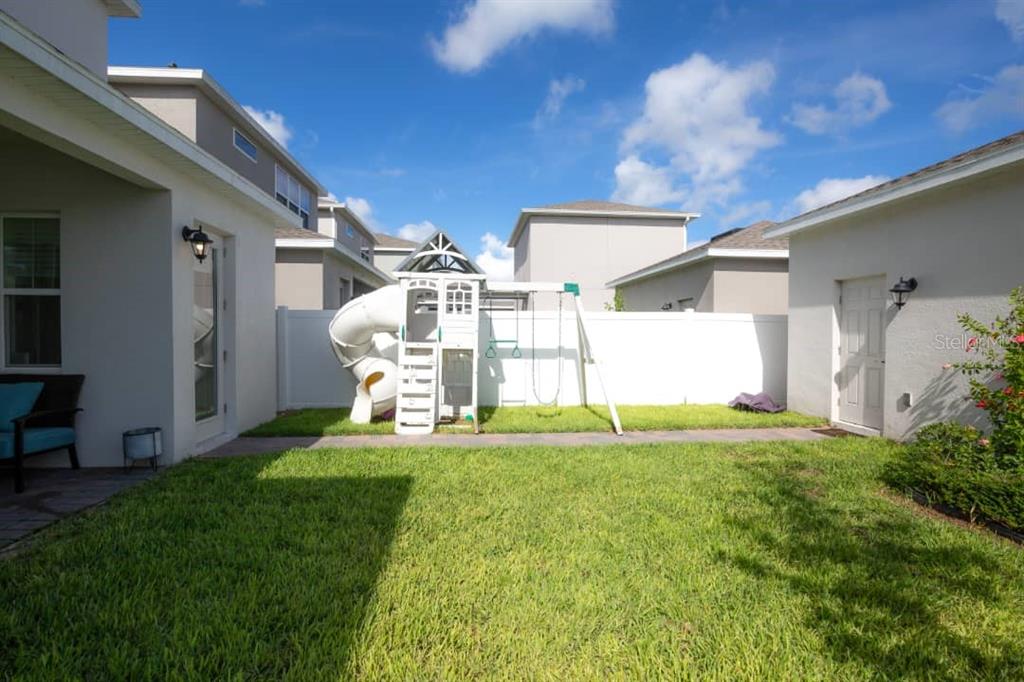 A backyard features a white playset with a slide and swings against a privacy fence — 15367 GILLIGAN COURT, WINTER GARDEN, FL