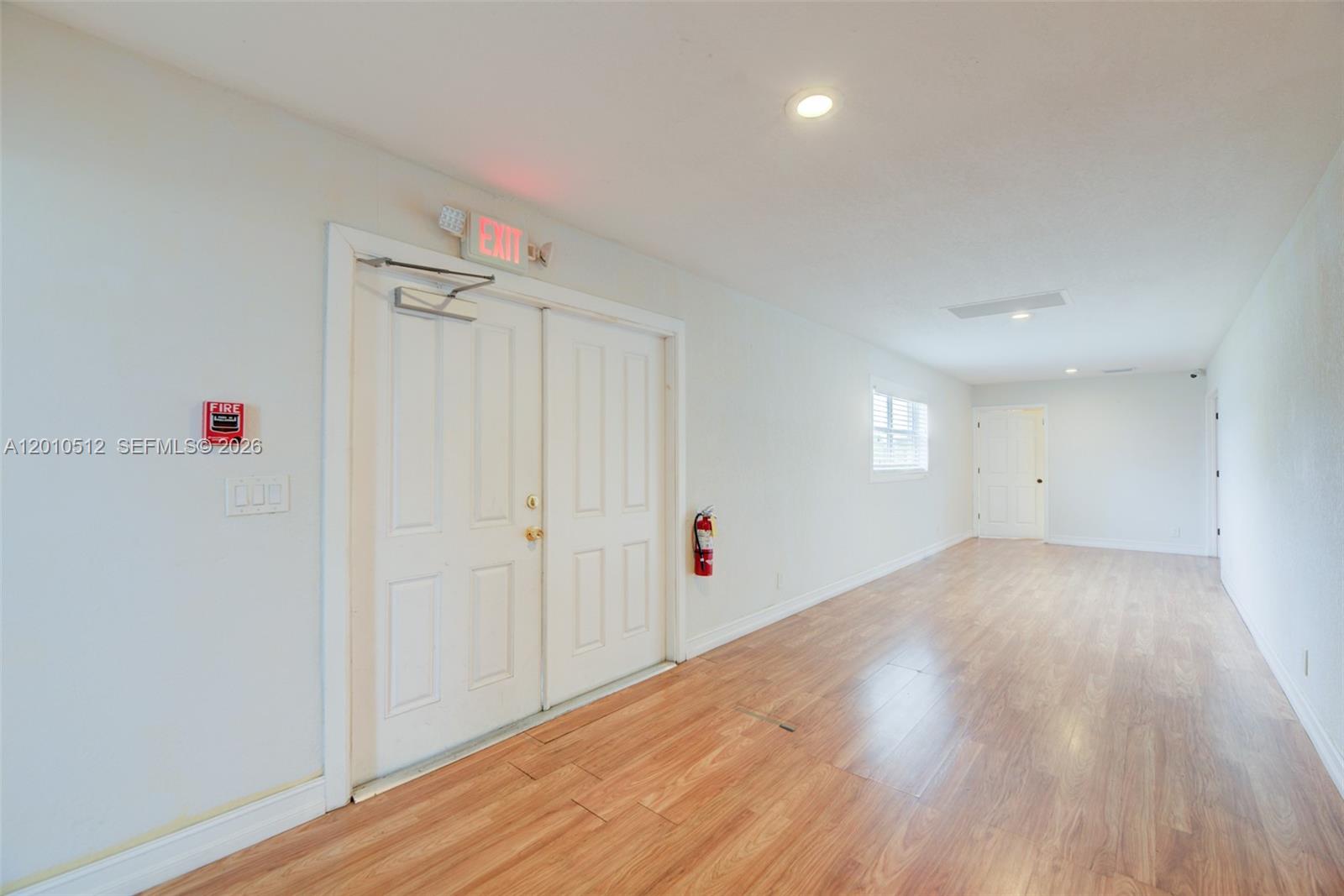 A long, empty room features light wood-look flooring, white walls, double exit doors, and recessed lighting — 359 10th St, Lake Park FL 33403, LAKE PARK, FL