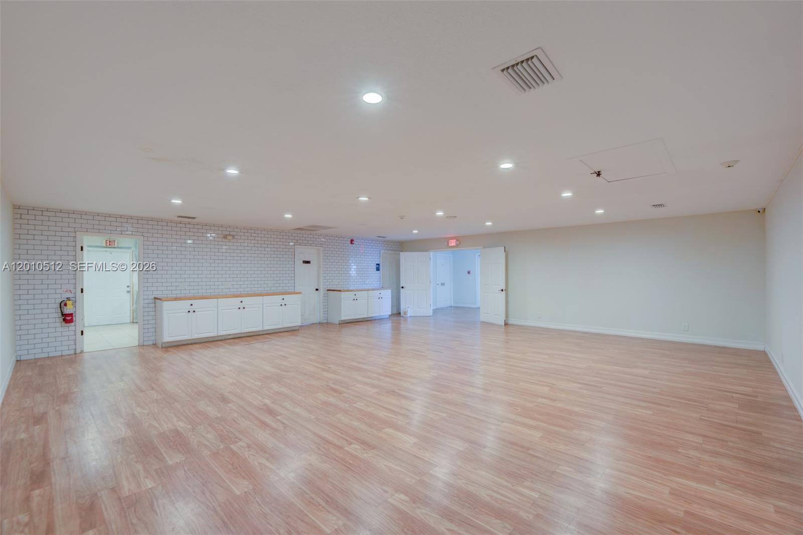 A large, empty room features light wood-look flooring, white subway tile walls, and white cabinetry — 359 10th St, Lake Park FL 33403, LAKE PARK, FL