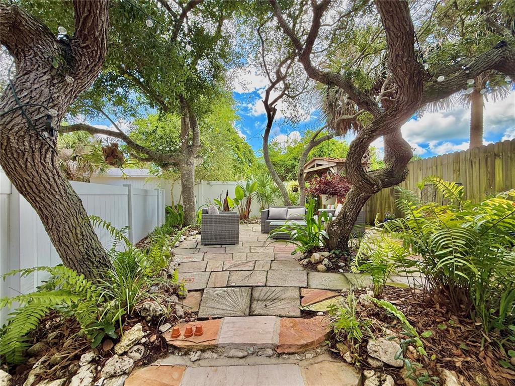 A stone patio with outdoor seating is nestled between large trees in a fenced backyard — 2023 S FLAGLER AVENUE, FLAGLER BEACH, FL