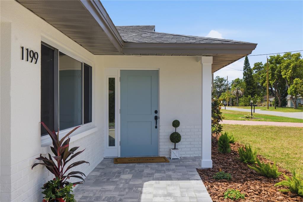 A light blue front door with a side window sits under a covered porch entrance — 1199 KEENE ROAD, DUNEDIN, FL