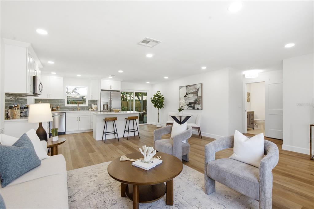An open-concept living room and kitchen featuring white cabinetry, wood flooring, and neutral furniture — 1199 KEENE ROAD, DUNEDIN, FL
