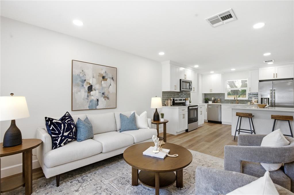 A bright open-concept living room and kitchen featuring white cabinetry, wood flooring, and neutral furniture — 1199 KEENE ROAD, DUNEDIN, FL