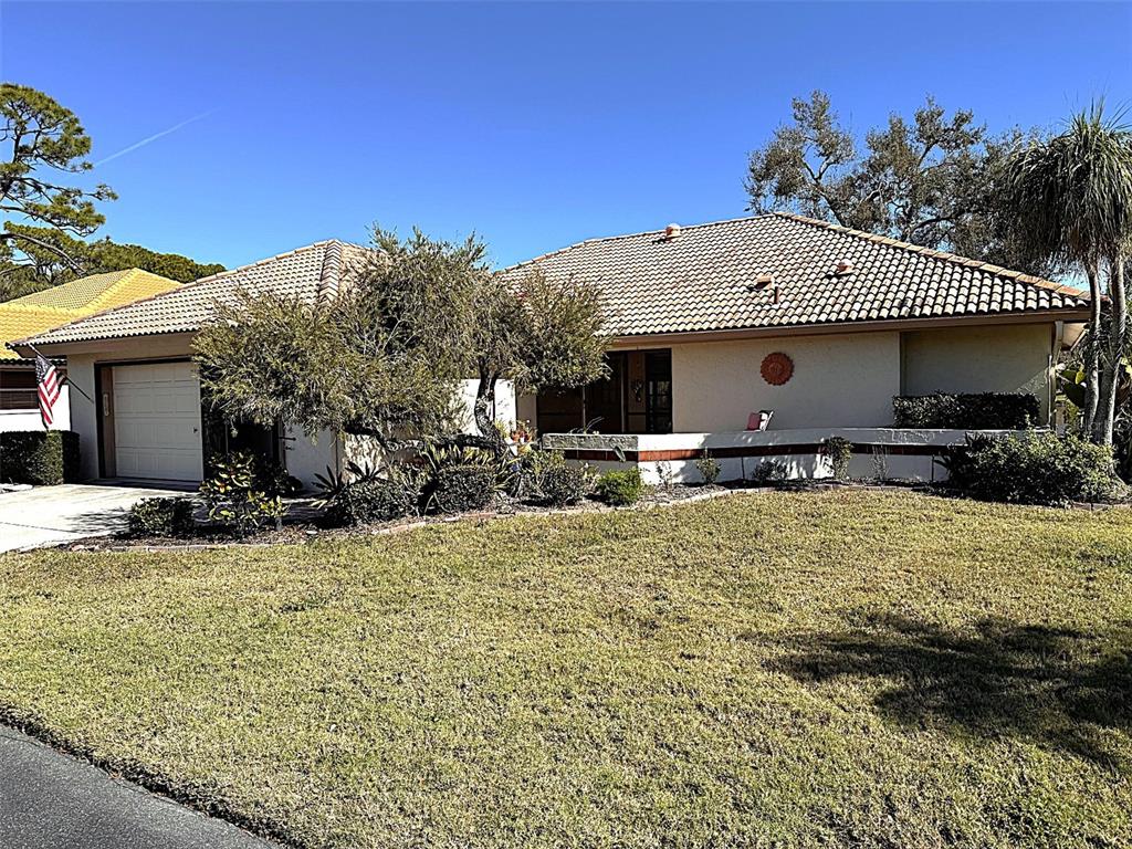 A single-story house with a tiled roof, garage, and front yard landscaping under a blue sky — 229 LAUREL HOLLOW DRIVE UNIT 83, NOKOMIS, FL