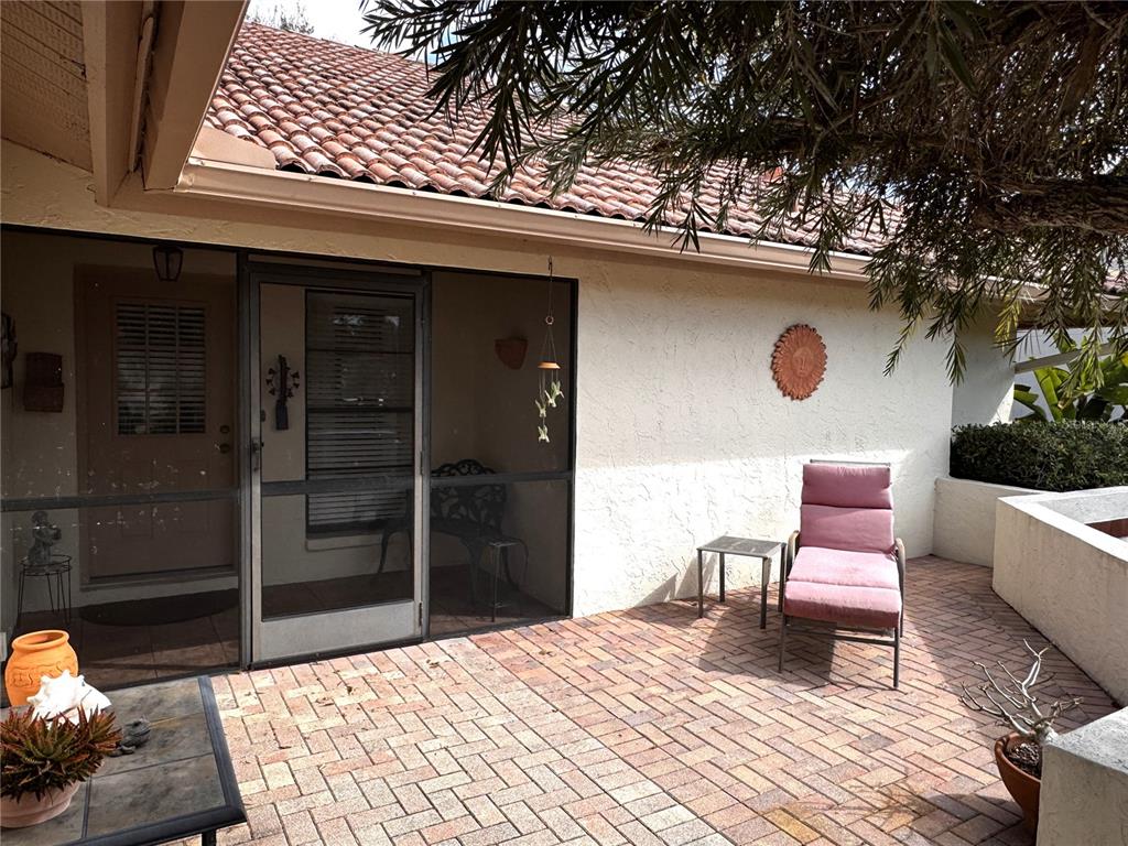 A brick patio features a lounge chair, a small table, and a screened-in entryway — 229 LAUREL HOLLOW DRIVE UNIT 83, NOKOMIS, FL