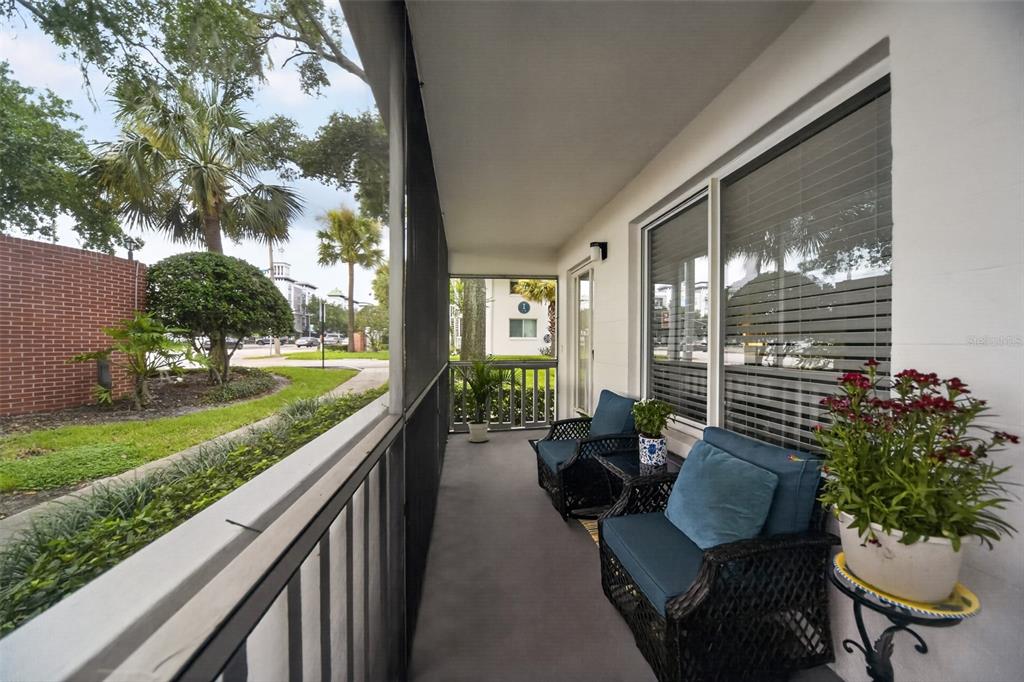 A screened-in porch features two wicker chairs, a small table, and a view of landscaping — 1140 S ORLANDO AVENUE UNIT E1, MAITLAND, FL