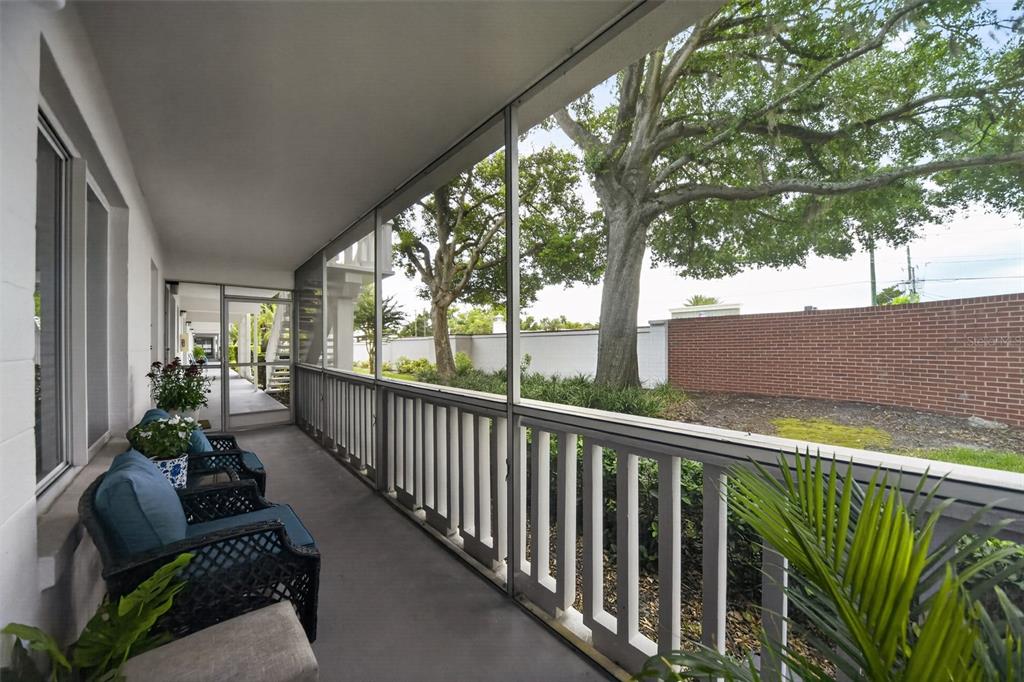 A screened-in porch features wicker chairs, a concrete floor, and views of trees and brick — 1140 S ORLANDO AVENUE UNIT E1, MAITLAND, FL