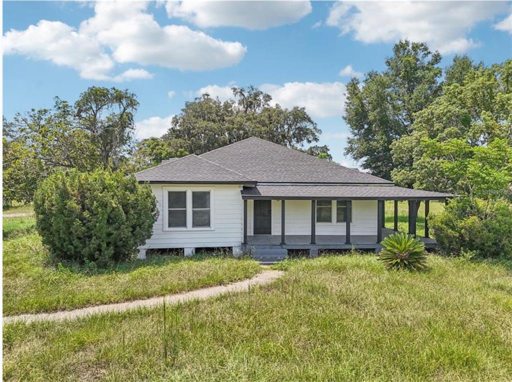 A white, single-story house with a dark roof and a front porch sits in grass — 41333 STATE ROAD 19, UMATILLA, FL