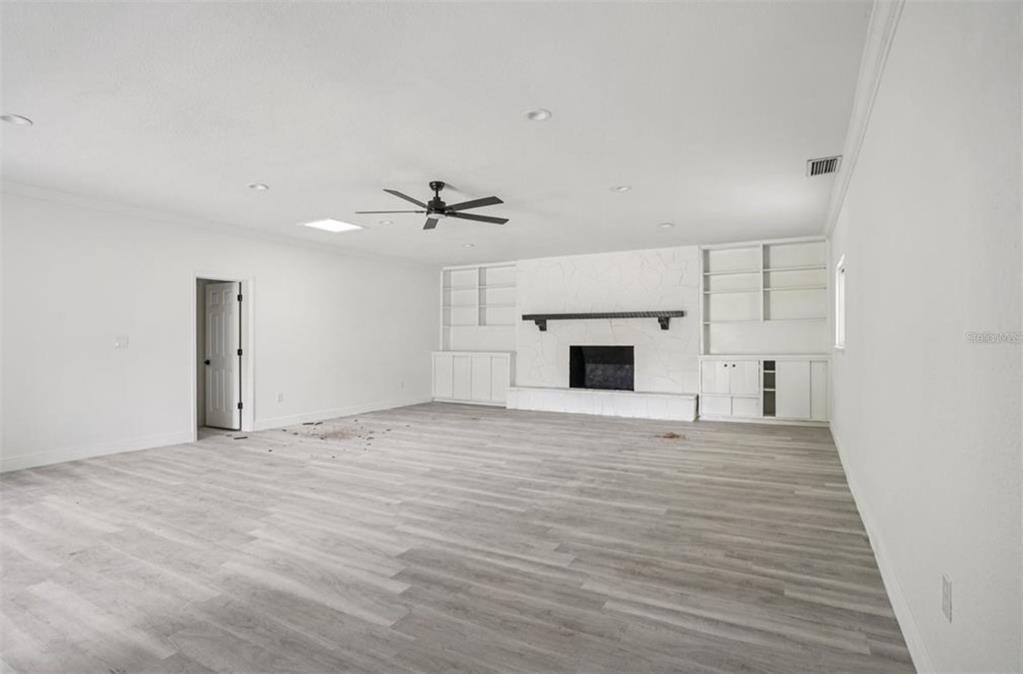 A spacious living room features white walls, light wood-look flooring, and a white stone fireplace — 41333 STATE ROAD 19, UMATILLA, FL