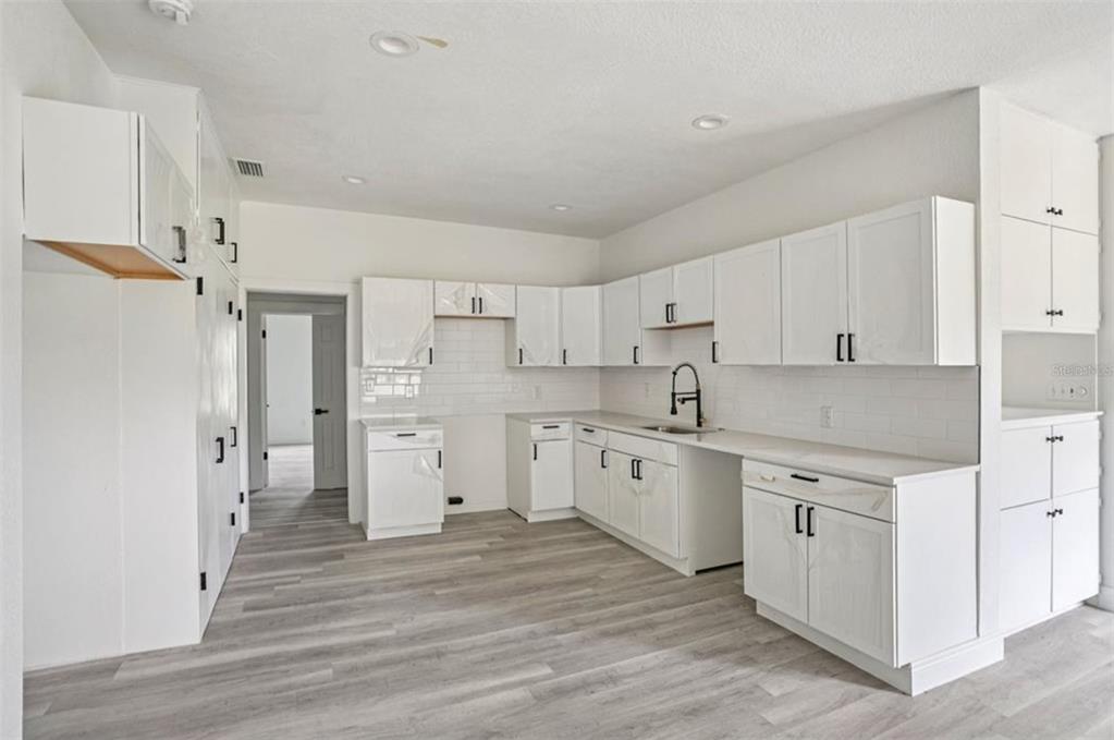 A kitchen features white cabinets, light wood-look flooring, and a white subway tile backsplash — 41333 STATE ROAD 19, UMATILLA, FL