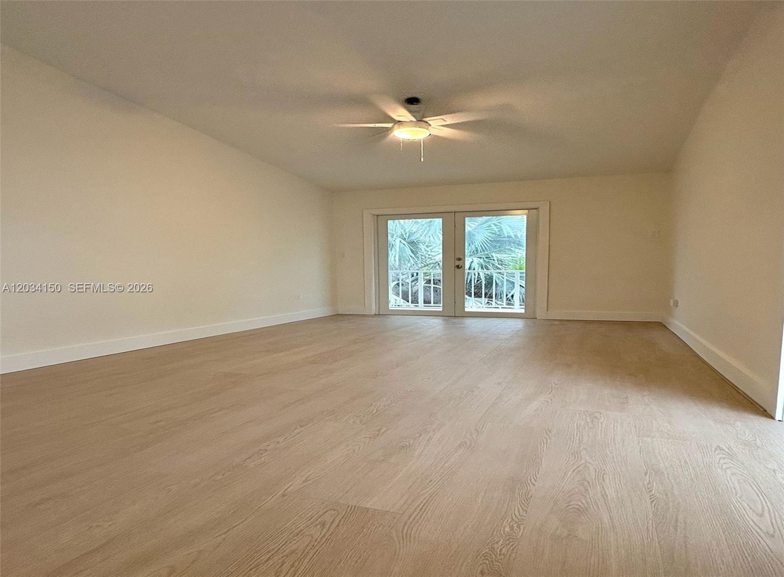 An empty room features light wood-look flooring, white walls, a ceiling fan, and glass doors — 136 Marina Ave, Key Largo FL 33037, KEY LARGO, FL