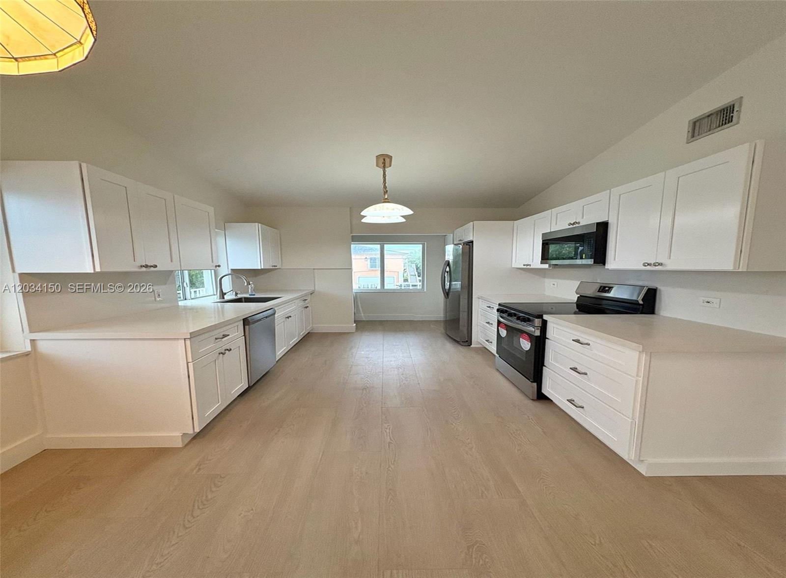 A bright kitchen features white cabinets, stainless steel appliances, and light wood-look flooring — 136 Marina Ave, Key Largo FL 33037, KEY LARGO, FL