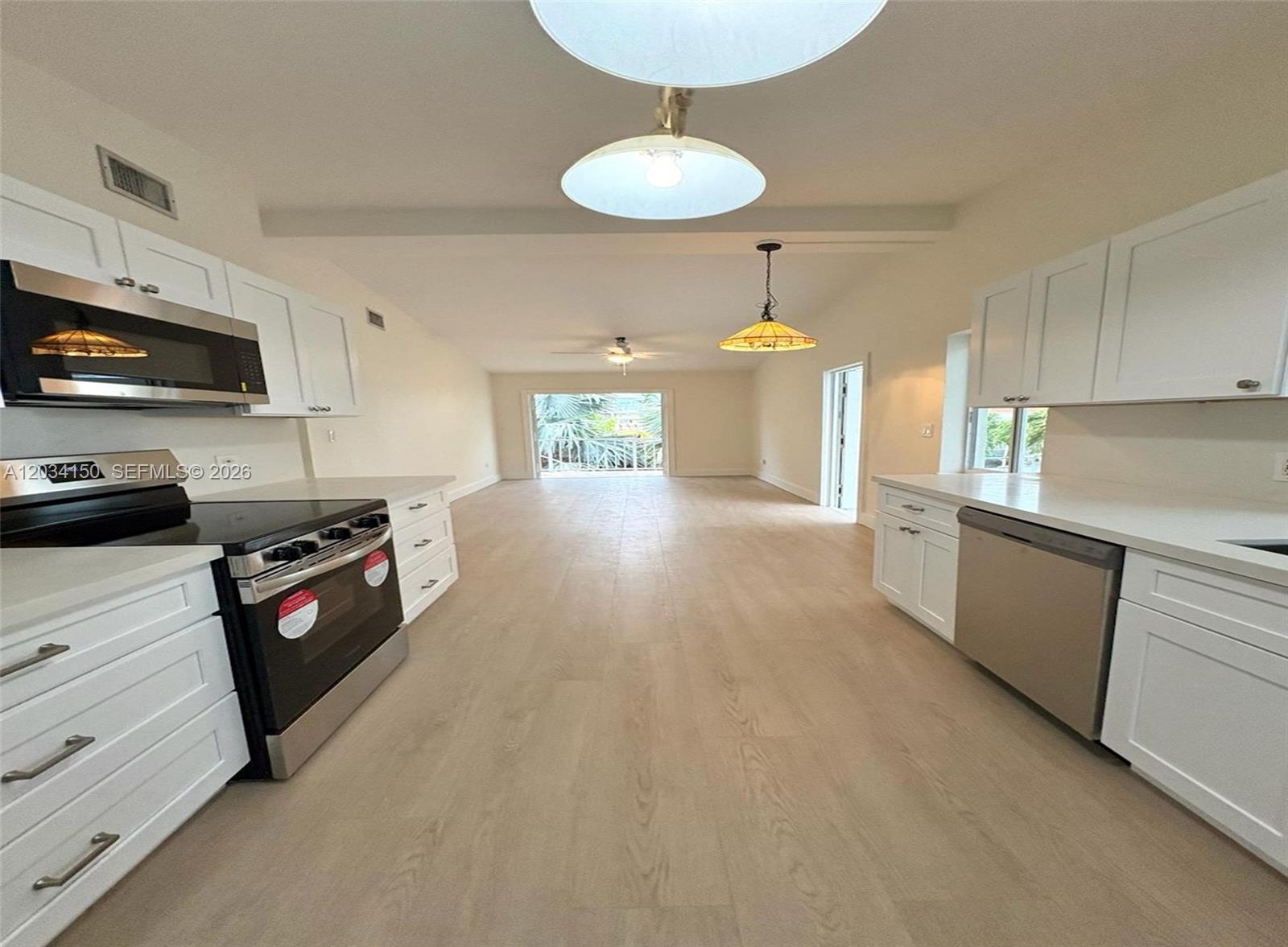 A kitchen with white cabinets and stainless steel appliances opens into a living area — 136 Marina Ave, Key Largo FL 33037, KEY LARGO, FL