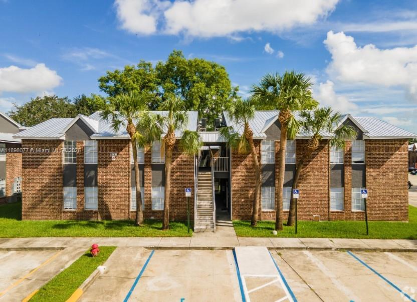 A two-story brick apartment building features a central staircase and palm trees in front — 2000 S Main Street # 000, Belle Glade FL 33430, BELLE GLADE, FL