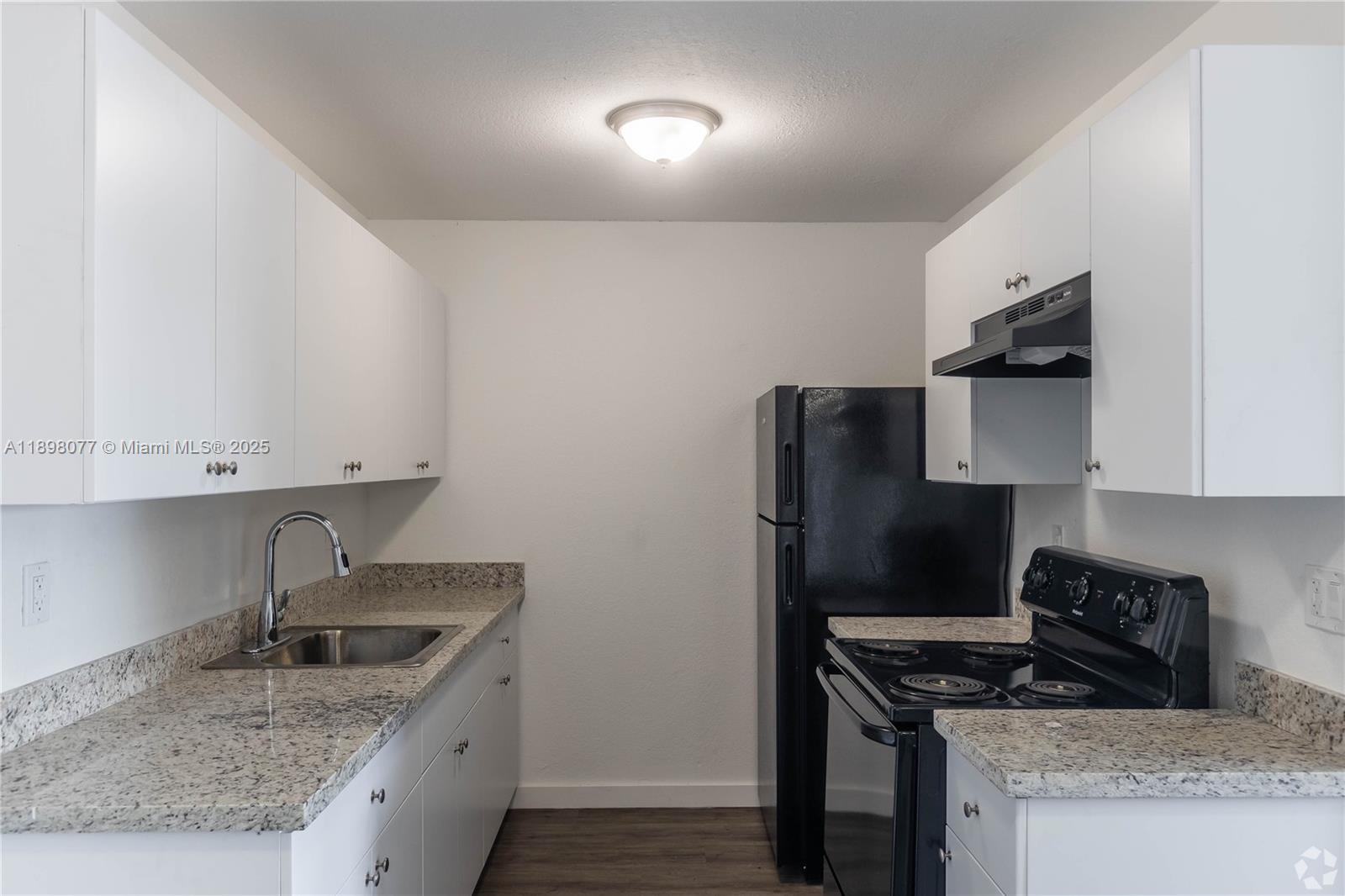 A galley kitchen features white cabinets, granite countertops, and black appliances — 2000 S Main Street # 000, Belle Glade FL 33430, BELLE GLADE, FL