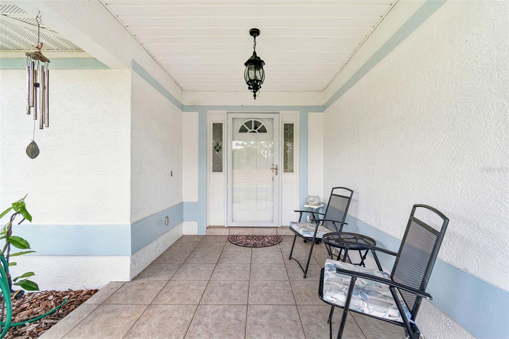 A covered front porch features tiled flooring, two chairs, and a glass-paneled front door — 6353 SILVER LAKES DRIVE W, LAKELAND, FL