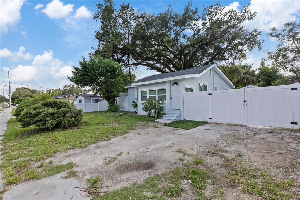 A light blue house with a white fence and a gravel driveway under large trees — 8714 N BLVD, TAMPA, FL