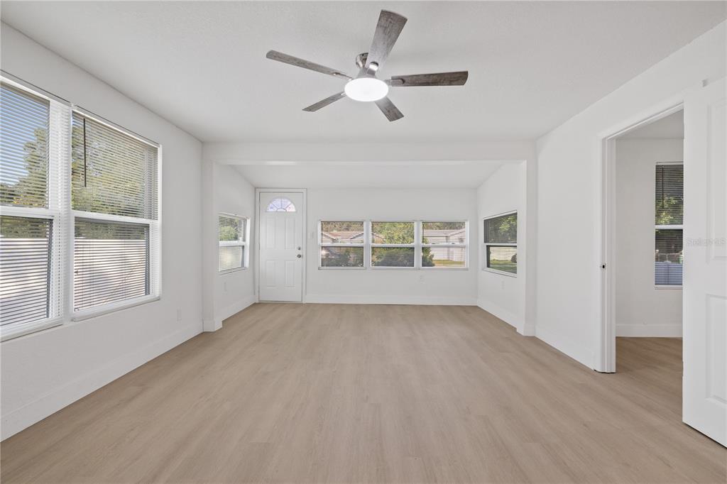 A bright, empty room features light wood-look flooring, white walls, and a ceiling fan — 8714 N BLVD, TAMPA, FL